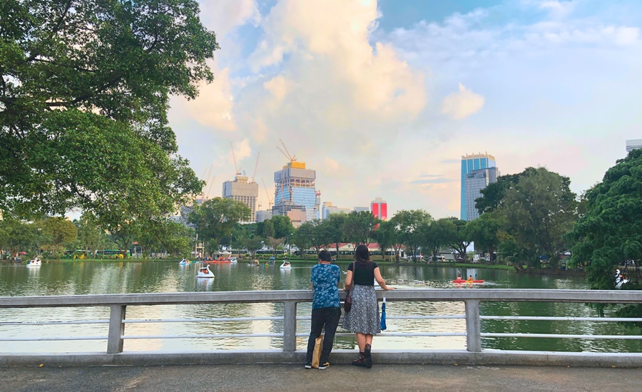 couple stand on bridge looking over lumpini park lake swan boats in the background bangkok thailand