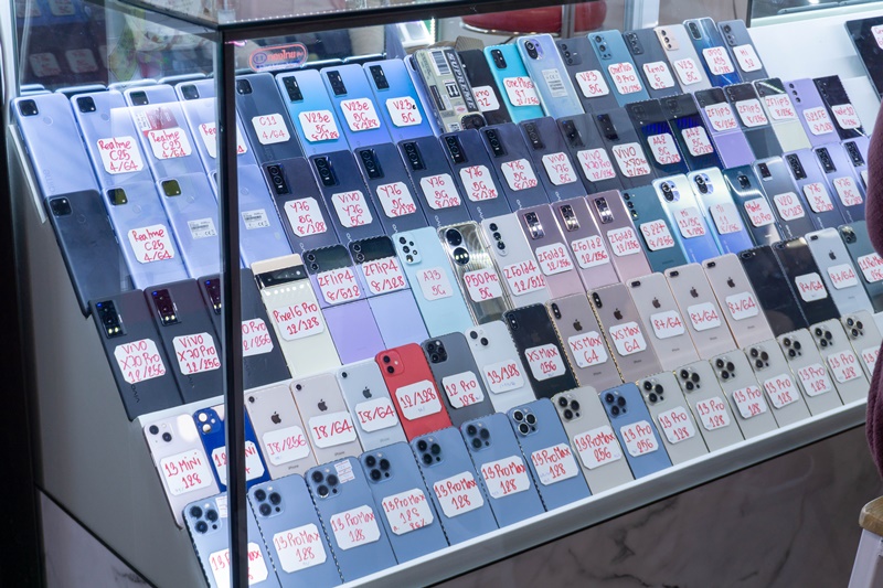 iPhone and Samsung model mobile phones laid out on display in a glass cabinet at the MBK Center in Bangkok