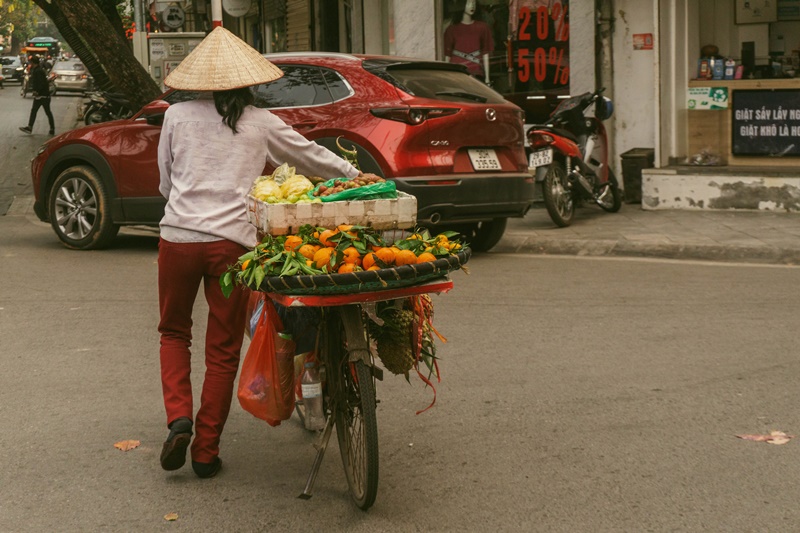 vietnam fruit seller on bike in hanoi and wears hanoi vietnam hat