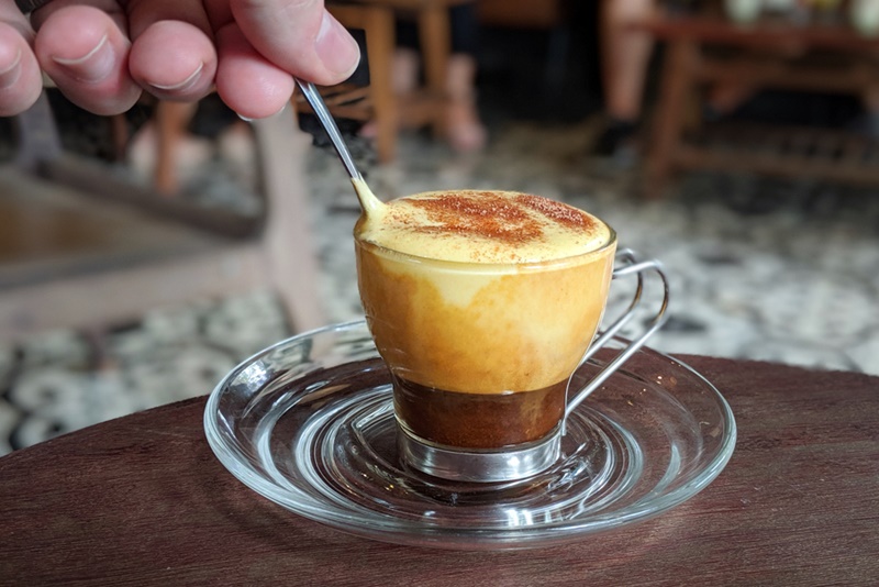 you have to try the egg coffe in Hanoi photo shows a glass of vietnam egg coffe being stired