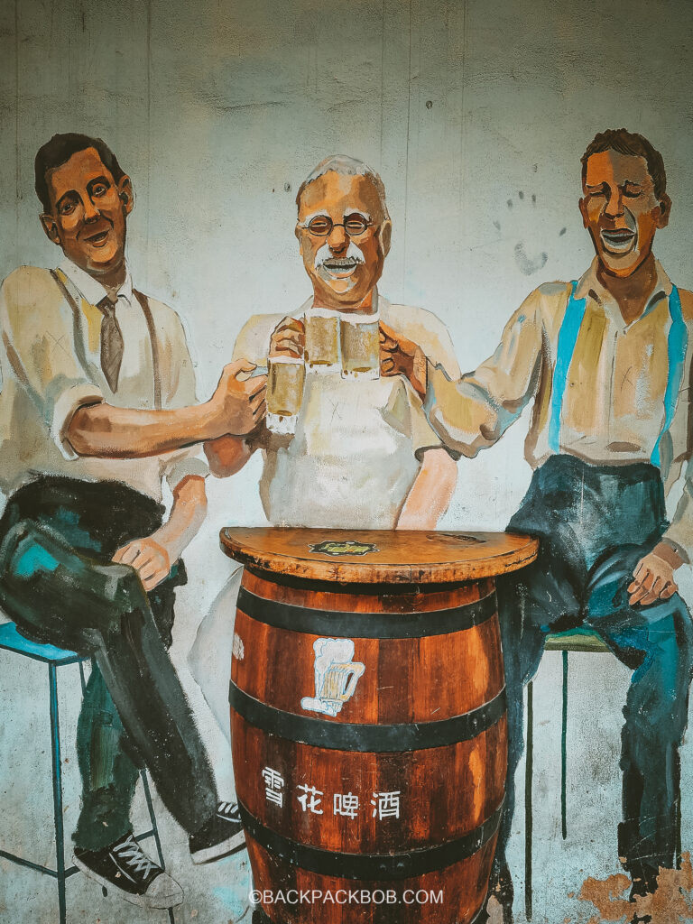street art painted on the wall in Ipoh, three men sat around an Ipoh barrel table and drink Ipoh beer