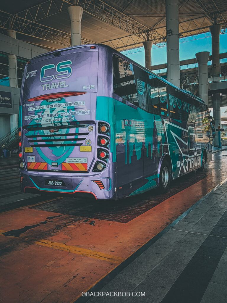 A blue and purple bus arrives at Kuala Lumpur bus terminal there is writing on the bus and the company name in CS Travel. Passengers pay a low price for their tickets
