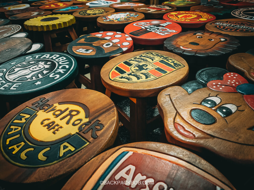 A collection of handmade wooden stools for sale at Jonker Market. Stools are decorated with logos from well know brands such as the Hard Rock Cafe, melaka Jonkers Street Market | Jonkers Street Weekend Market | Jonkers Street Night Market | Jonkers Street Market in Melaka