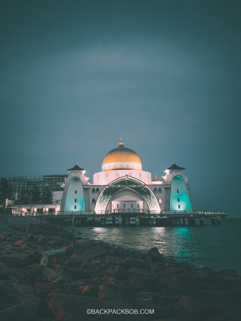 taking a photo of the Melaka straits mosque on Malaysia itinerary the photo is taken at night from the beach and the mosque is illuminated with blue light