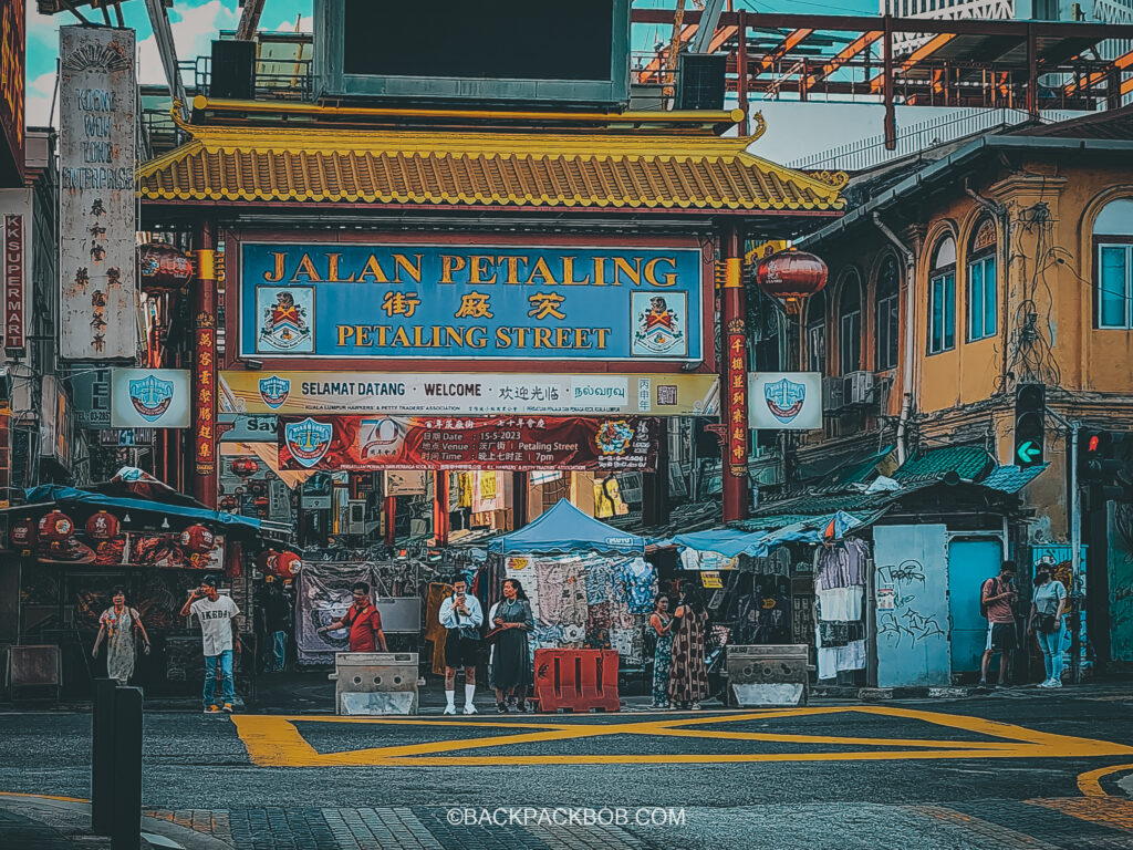 Petaling Street market, a free thing to do in Kuala Lumpur has a red archway and huge blue sign which reads Jalan Petaling over the entrance