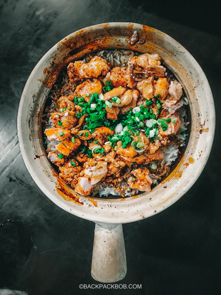 A Kuala Lumpur Malaysia itinerary Chicken clay pot. The clacypot which is cooked on a high heat contains rice chicked and a spring onion garnish