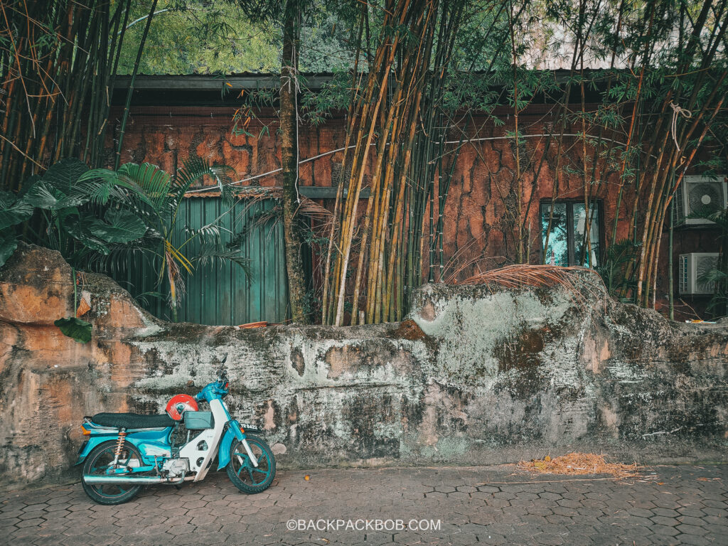 A motorcycle is parked at the Batu Cave Temple and bamboo grows near the cave entrance