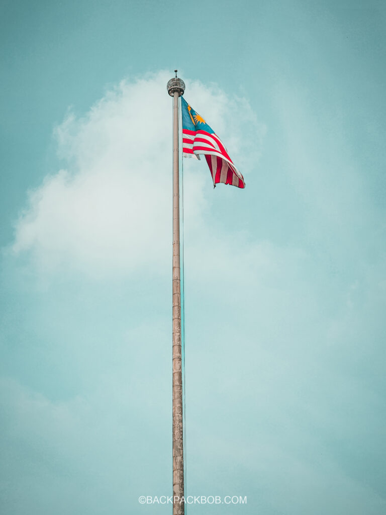 the free flagpole is standing in Merdeka square, a free attraction to visit in Kuala Lumpur. The famous flag is at full mast the flag is Malaysian and the background is all sky which is bright nlur
