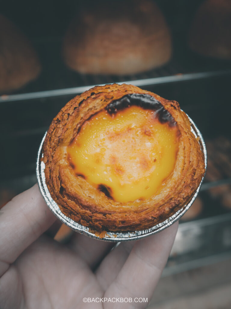 Backpack bob holds an egg tart after buing it at the Jonker Street Market in Melaka Malaysia Jonkers Street Market | Jonkers Street Weekend Market | Jonkers Street Night Market | Jonkers Street Market in Melaka