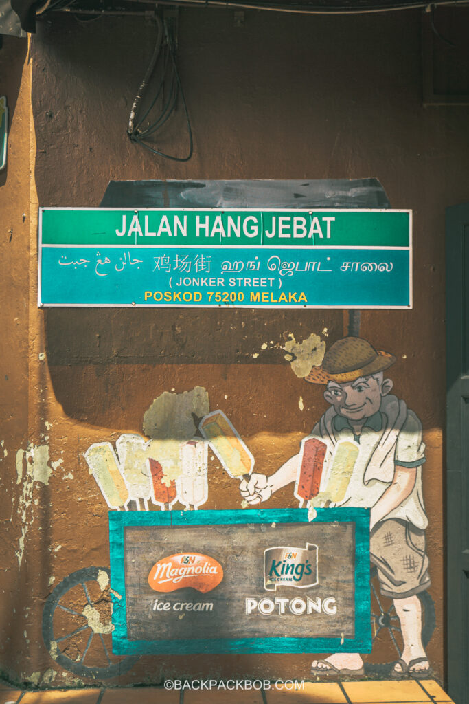 Street art on Jonkers Street pictures an ice cream seller with a cart. The official Jonkers Street Sign is painted above and reads "Jalan Hang Jebat (Jonkers Street), Poskof 75200 Melaka. Jonkers Street Market | Jonkers Street Weekend Market | Jonkers Street Night Market | Jonkers Street Market in Melaka