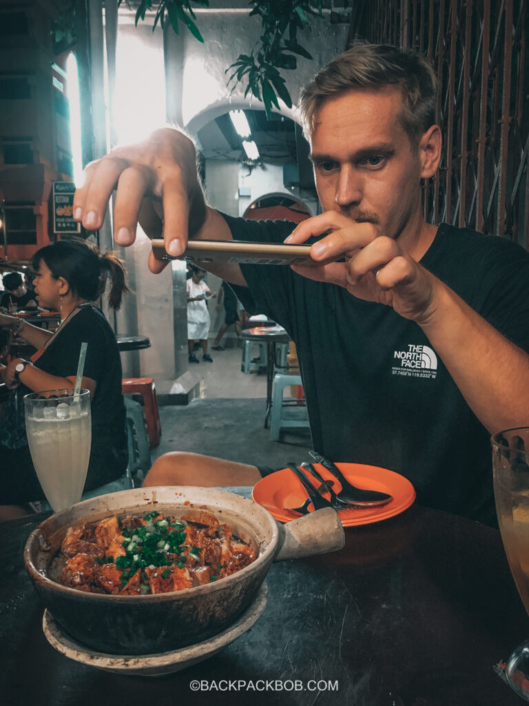 Backpack bob concentrates too hard while taking a free photo of the chicken claypot in Kuala Lumpur