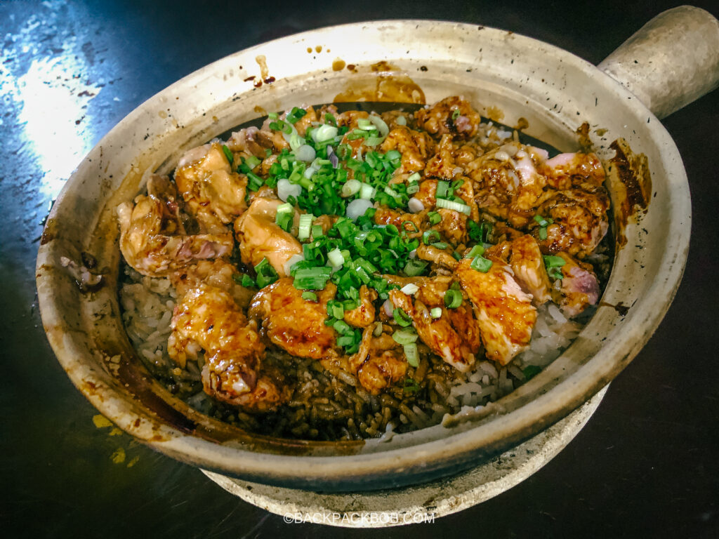 A chicken claypot is a cheap dinner in Kuala Lumpur and it is a local delicacy this photo shows a medium size clay pot filled with rice and chicken, the pot is garnished with green spring onions in Kuala Lumpur