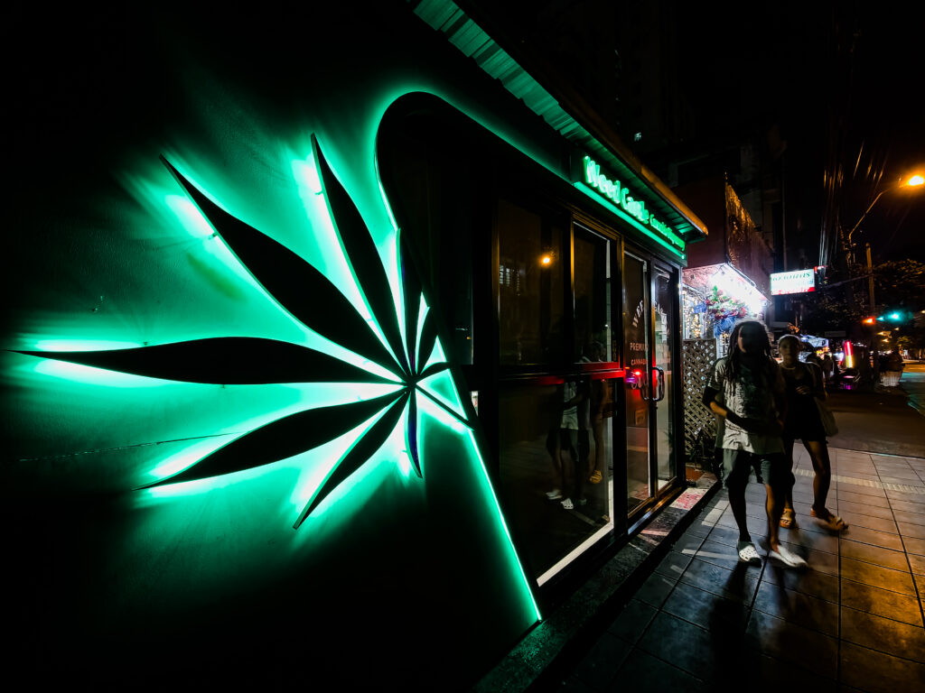 A legal cannabis store in Thailand with a green cannabis leaf sign outside. Tourists are buying legal weed from the store